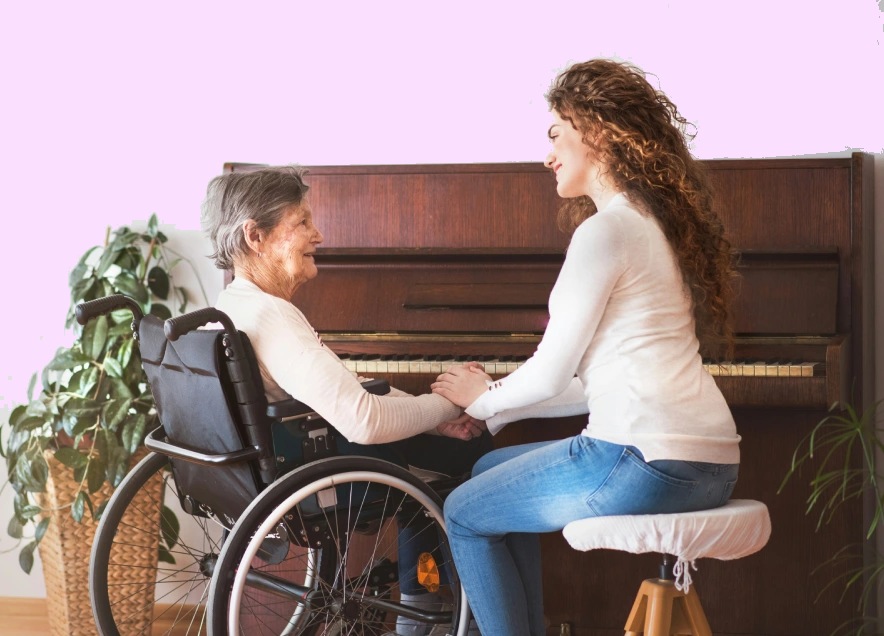 A woman in a wheelchair smiles while holding hands with another woman seated on a stool in front of a piano.